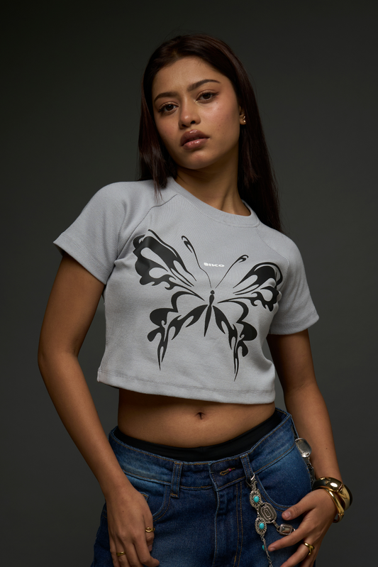 A woman wearing a gray crop top with a butterfly graphic and blue jeans.